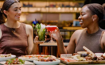 Two women in a restaurant with drinks in hand and meals on the table