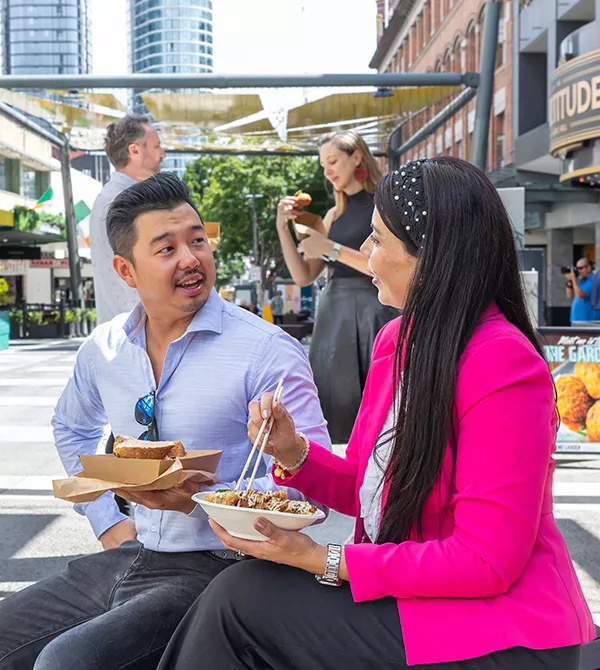 Man in a blue shirt and woman in a pink top eating lunch in Brunswick Street Mall. 
