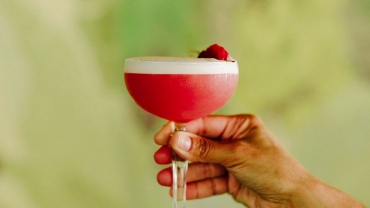 Hand holding pink cocktail against green background