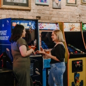 Two girls standing holding beers in front of arcade machines